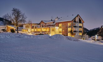 Ein gemütliches Hotel in einer verschneiten Landschaft. Der Abendhimmel ist klar und die Gebäude sind schön beleuchtet.