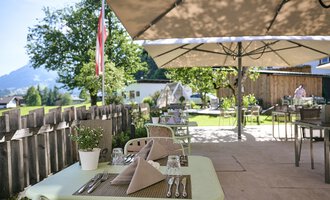 A cozy terrace with tables and sunshades. In the background, trees and a picturesque landscape can be seen. | © Alexander Kaiser