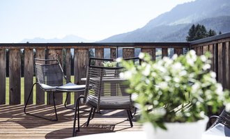A cozy terrace with modern chairs and a view of the mountains. In the foreground, there is a pot with green plants. | © Alexander Kaiser