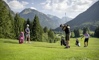 A group of golfers is practicing on a picturesque golf course with mountains in the background. The sun is shining, and the landscape is green and inviting. | © Golfclub Oberstdorf | ©kunst.joachimweiler.de