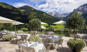 Ein stilvolles Restaurant im Freien mit Blick auf die Berge. Es gibt elegante Tische mit Sonnenschirmen und grüne Pflanzen. | © Hallers Geniesserhotel | Dietmar Walser