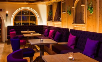 An inviting restaurant with cozy seating areas and warm wood interiors. The purple cushions on the benches create a relaxed atmosphere. | © Haller's Geniesserhotel | Dietmar Walser