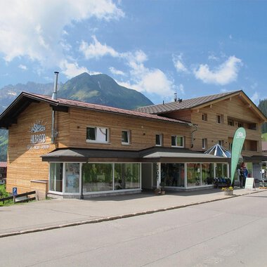 Ein modernes Holzgebäude in einer malerischen Berglandschaft. Die klare Himmel und die umgebenden Berge verleihen dem Ort einen einladenden Charakter. | © Sport Hilbrand OG