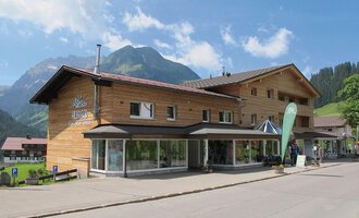 Ein modernes Holzgebäude in einer malerischen Berglandschaft. Die klare Himmel und die umgebenden Berge verleihen dem Ort einen einladenden Charakter. | © Sport Hilbrand GmbH
