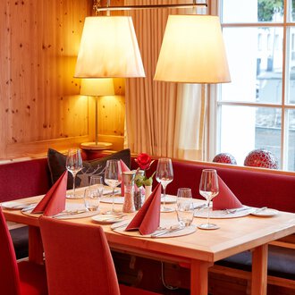 Ein einladendes Restaurant mit Holzdekoration und gemütlicher Atmosphäre. Der Tisch ist elegant gedeckt und mit roten Servietten dekoriert. | © Hotel Riezler Hof | M. Hasterok