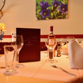 © IFA Breitach Apartements A beautifully set table in an elegant restaurant. On the table are glasses, a wine bottle, and a menu. | © IFA Breitach Apartements