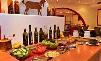 A beautifully decorated buffet area with fresh food and various bottles of oil. In the background, there is a wall decoration featuring a goat. | © IFA Breitach Apartements