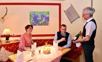 Ein schickes Restaurant mit einem gemütlichen Ambiente. Ein Kellner serviert einem Paar am Tisch eine Flasche Wein. | © IFA Breitach Apartements