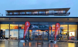 Ein modernes Ski- und Sportgeschäft mit großen Fenstern. Rote Fahnen mit der Aufschrift „Ski Center“ stehen vor dem Eingang. | © Ifensport | Thomas MARTIN