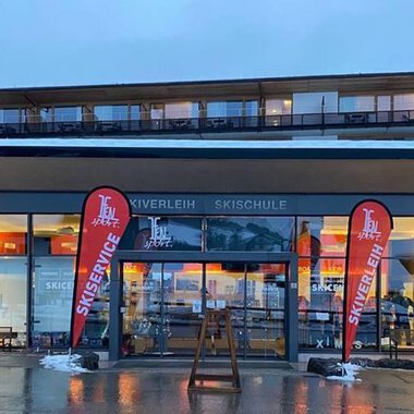 Ein modernes Ski- und Sportgeschäft mit großen Fenstern. Rote Fahnen mit der Aufschrift „Ski Center“ stehen vor dem Eingang. | © Ifensport | Thomas MARTIN
