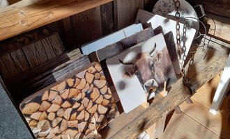 Eine Holzbank mit mehreren Bildern, die Holzstämme und ein Rind zeigen. Die Umgebung wirkt rustikal und gemütlich. | © iKuh Schöne Ideen | Daniela Neumann