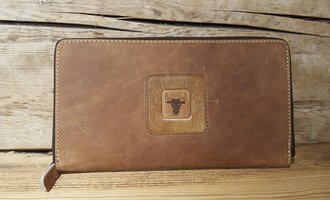 A brown leather wallet with an embossed motif of a bull. The background is a rustic wooden surface.