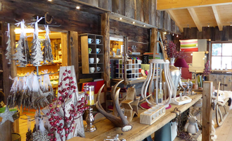 Ein gemütlicher Shop mit rustikalen Holzmöbeln und dekorativen Artikeln. Es gibt eine Vielzahl von Weihnachts- und Wohnaccessoires auf den Regalen.
