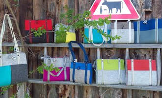 A row of colorful bags hangs on a wooden shelf next to a warning sign for cows. The bags are made from various materials and colors.