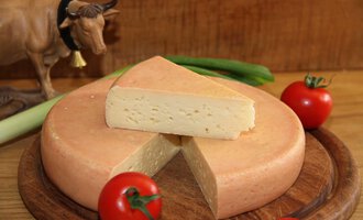 Ein Käselaib mit einer abgeschnittenen Scheibe liegt auf einem Holzbrett. Darum sind frische Tomaten und eine Kuhfigur zu sehen. | © Innere Wiesalpe | Andrea Kainz zuckerschnecke.at