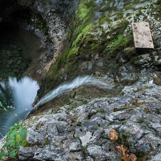 © Kleinwalsertal Tourismus | Andre Tappe Eine felsige Klippe mit fließendem Wasser, das in einen tiefen, dunklen Pool mündet. Grüne Moose und Pflanzen wachsen zwischen den Steinen. | © Kleinwalsertal Tourismus | Andre Tappe