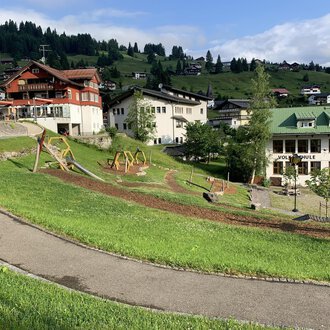 © Kleinwalsertal Tourismus | A picturesque landscape with green meadows and playgrounds. In the background, some chalet-like buildings and mountains can be seen. | © Kleinwalsertal Tourismus |