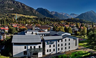 Ein modernes Gebäude umgeben von Bergen und Bäumen. Der Himmel ist klar und die Umgebung wirkt ruhig und einladend. | © Klinikverbund Allgäu