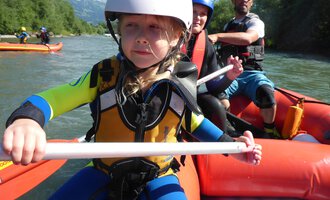 Ein Kind in einem Ruderboot trägt einen Helm und eine Schwimmweste. Im Hintergrund sind weitere Bootsfahrer auf einem Fluss zu sehen. | © MAP-Erlebnis