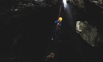 Ein Kletterer hängt an einem Seil in einer dunklen Schlucht. Wasser fällt herab und sorgt für eine aufregende Atmosphäre. | © MAP-Erlebnis