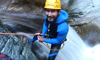 Ein Mann in einem blauen Neoprenanzug klettert an einem Wasserfall. Er trägt einen Helm und ist mit einem Seil gesichert. | © MAP-Erlebnis