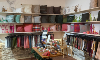 A cozy store with shelves full of decorative cushions in various colors and patterns. Below are colorful fabrics and accessories for sale on display. | © Herzstichle | Ninja Matt