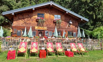 Ein traditionelles Holzhaus umgeben von Bäumen. Vor dem Haus stehen Liegestühle und Sonnenschirme in einer freundlichen Atmosphäre. | © Maxhütte | Viera Krafcik