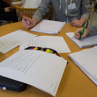 A group of people is working at a table with notes and writing materials. Various sheets and notebooks are on the table. | © Kleinwalsertal Tourismus