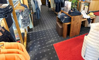 Ein gut sortierter Bekleidungsgeschäft mit verschiedenen Textilien und Accessoires. Der Holzboden und die warme Beleuchtung schaffen eine einladende Atmosphäre. | © Moosbrugger Mode e.U.