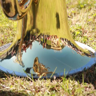 Eine glänzende Trompete, die auf dem Gras steht. Im reflektierenden Metall sind Bäume und Menschen zu sehen. | © Kleinwalsertal Tourismus | Frank Drechsel