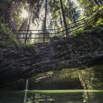 Ein idyllischer Ort mit klaren Gewässern und steilen Felsen. Im Hintergrund sind hohe Bäume und ein Sonnenstrahl sichtbar. | © Kleinwalsertal Tourismus | Oliver Farys