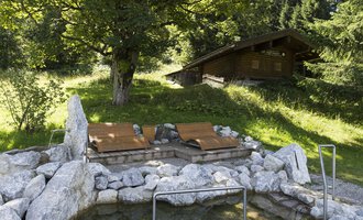 Ein ruhiger Ort mit einer Außensauna und Liegen, umgeben von Natur. Im Hintergrund steht ein Holzhaus zwischen Bäumen. | © Kleinwalsertal Tourismus | Oliver Farys