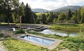 A small pool in a green environment with trees and a calm water surface in the background. The landscape is gently rolling and invites relaxation. | © Kleinwalsertal Tourismus | Veronika Senn