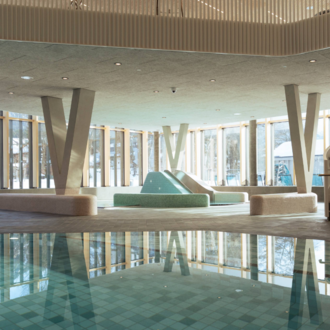 A modern swimming pool with crystal-clear water and elegant design. People are relaxing in the water and enjoying the atmosphere. | © Tourismus Oberstdorf