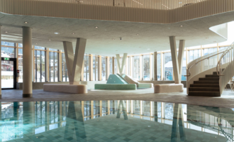 A modern swimming pool with crystal-clear water and elegant design. People are relaxing in the water and enjoying the atmosphere. | © Tourismus Oberstdorf