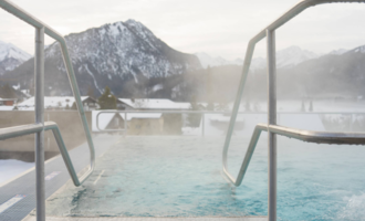 A modern wellness area with comfortable loungers and large windows. People in bathrobes are relaxing and enjoying the tranquil atmosphere. | © Tourismus Oberstdorf