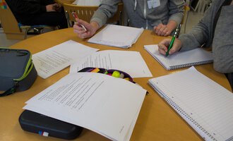 A group of people is sitting at a table and working on documents. Writing, notes, and writing materials are clearly visible. | © Kleinwalsertal Tourismus