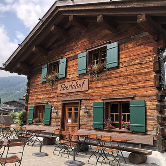 Ein traditionelles Holzhaus mit grünen Fensterläden und Blumen. Der Eherlehof lädt mit Terrassenmöbel zum Entspannen ein. | © Kleinwalsertal Tourismus | Louisa Hieke