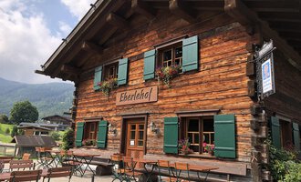 Ein traditionelles Holzhaus mit grünen Fensterläden und Blumen. Der Eherlehof lädt mit Terrassenmöbel zum Entspannen ein. | © Kleinwalsertal Tourismus | Louisa Hieke