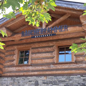 Ein gemütliches Holzhaus mit Fenster und einem dekorativen Schild. Umgeben von grünen Blättern und Bäumen. | © Kleinwalsertal Tourismus | Veronika Senn