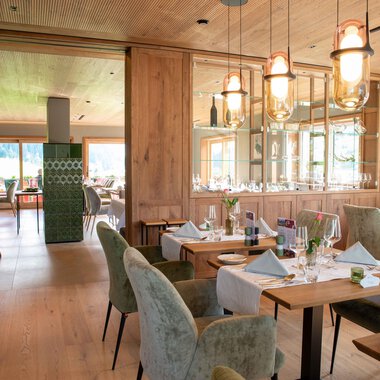 A modern restaurant with wooden decor and elegant tables. The space is bright and inviting, with cozy chairs and stylish lamps. | © Almhof Rupp | Lukas Kind