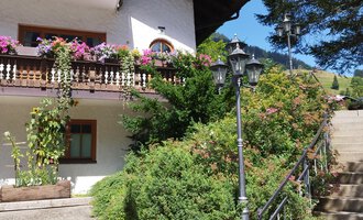 Ein schönes Haus mit blühenden Balkonen und begrünten Veranden. Die Treppe führt zu einem gepflegten Garten im Freien. | © Kleinwalsertal Tourismus | N. Lughammer