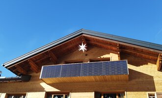 Ein modernes Holzhaus mit einem Balkon und Photovoltaik-Modulen. Der klare blaue Himmel sorgt für eine freundliche Atmosphäre. | © Kleinwalsertal Tourismus | N. Lughammer