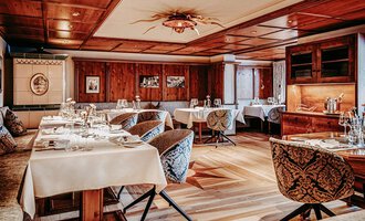 Ein elegantes Restaurant mit Holzvertäfelung und stilvollen Stühlen. Tische sind mit weißen Tischdecken und Geschirr gedeckt, das Ambiente ist gemütlich und einladend.