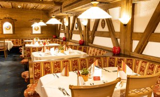 Ein gemütliches Restaurant mit Holzwänden und eleganter Tischdekoration. Bunte Tischdecken und warmes Licht schaffen eine einladende Atmosphäre. | © Hotel Alte Krone