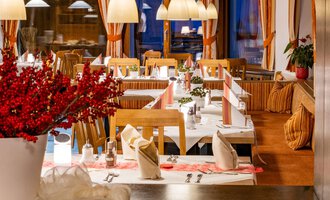 Ein gemütliches Restaurant mit elegant gedeckten Tischen und warmem Licht. Rote Akzente von Blumen und Dekorationen schaffen eine einladende Atmosphäre. | © Hotel Alte Krone