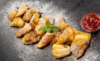 Eine köstliche Portion gebackener Teigstücke mit Puderzucker und frischer Minze. Dazu serviert ist ein Glas mit roter Marmelade. | © Hotel Alte Krone