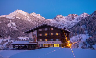 Ein gemütliches Berghaus im Schnee, umgeben von majestätischen Bergen. Der Himmel ist in sanften Blau- und lilatönen gefärbt. | © Hotel Alte Krone