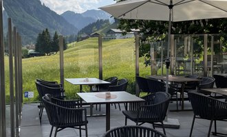 Eine einladende Terrasse mit schwarzen Stühlen und Tischen. Im Hintergrund sind grüne Wiesen und Berge unter einem blauen Himmel zu sehen. | © Robert Haller GmbH c/o Hotel Steinbock