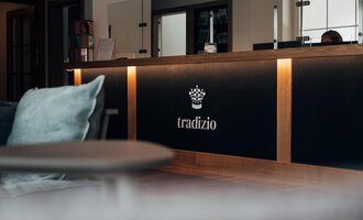 A modern reception area with an elegant reception desk. The logo "tradizio" is prominently displayed and appears inviting.